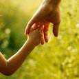 A little girl holding her dad's hand with tall grass in the background