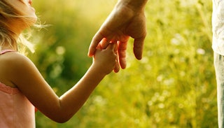 A little girl holding her dad's hand with tall grass in the background