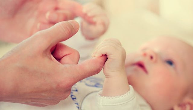 A child in the baby stage looking at his parent while holding his fingers