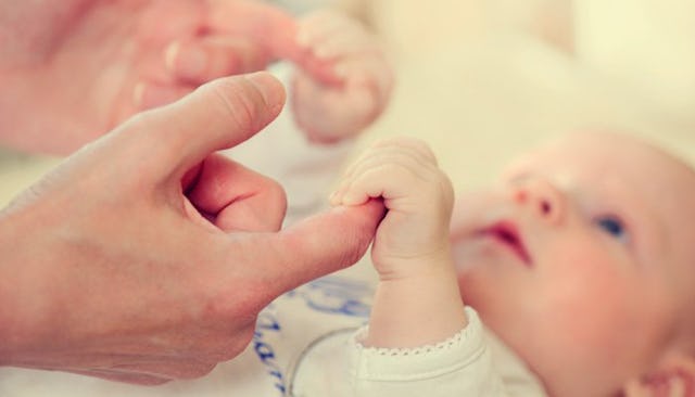 A child in the baby stage looking at his parent while holding his fingers 