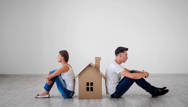 A divorced couple sitting with a cartoon house between them in an empty room