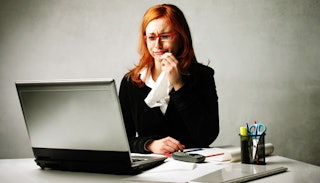 A woman sitting in front of her desk and laptop, looking worried and sad on her first day back at wo...
