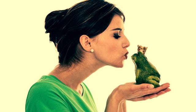 A side side profile of a woman in a green shirt kissing a frog