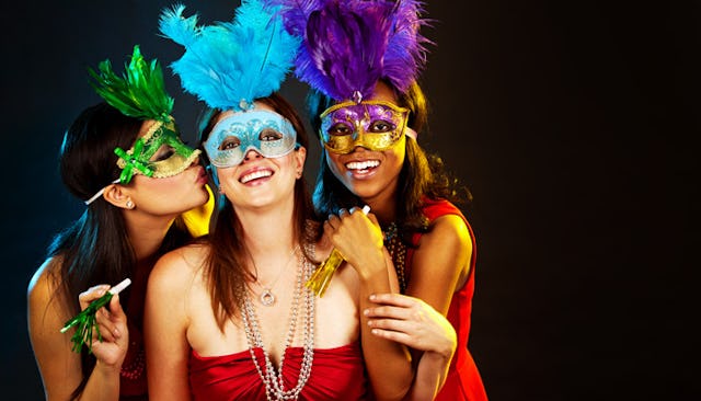 Three party girls with carnival masks standing together, posing and smiling
