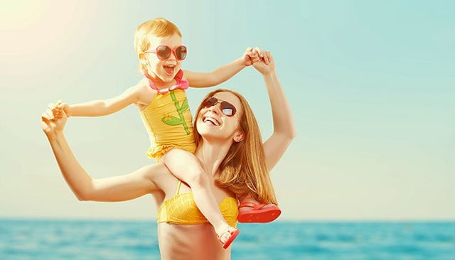 A girl in a yellow swimsuit with pink flower application sitting on her mother's shoulders while the...