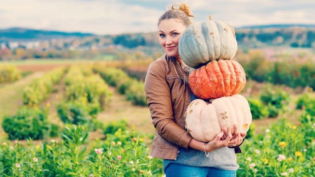 An autumn-loving woman in a brown jacket and blue denim jeans holding light yellow, orange, and gree...