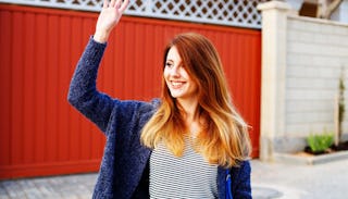 A ginger woman in a blue jacket smiling and waving at her neighbor