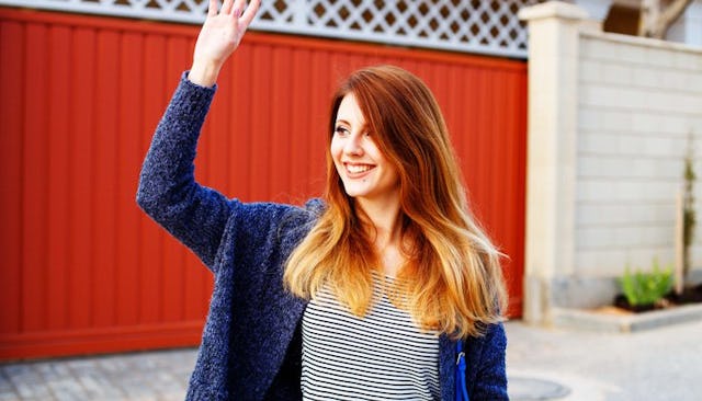 A ginger woman in a blue jacket smiling and waving at her neighbor