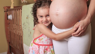 Little girl hugging her mum's pregnant stomach while having a big smile on her face because she's ex...