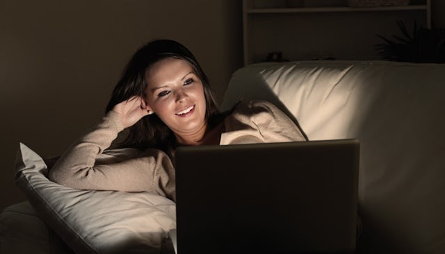 A young mother watching movies on her laptop in a dark room and smiling