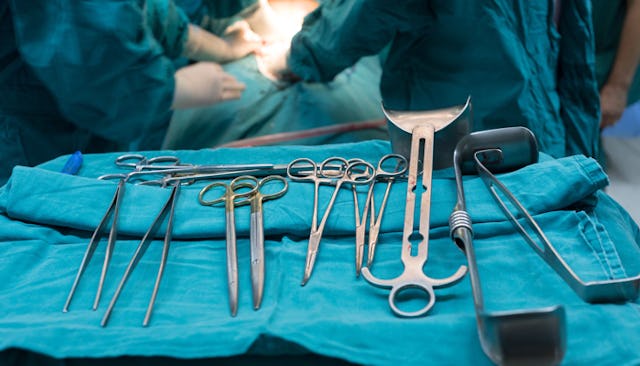 Several medical tools prepared on a blue fabric surface for a C-section surgery with doctors in the ...