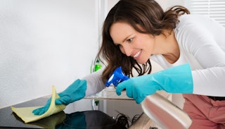 A good mom cleaning her kitchen with cleaning gloves, spray, and a cloth while smiling