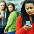 A young girl looking at her cellphone with a worried face after being bullied 