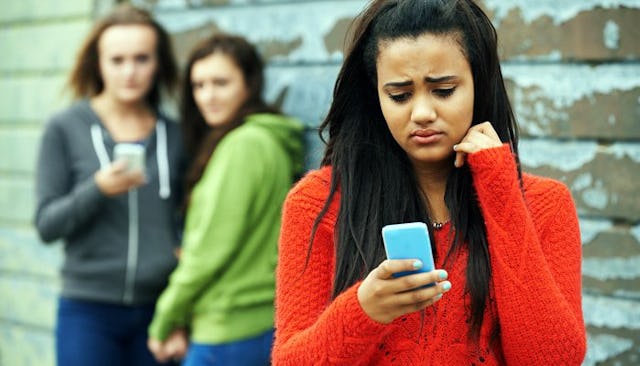 A young girl looking at her cellphone with a worried face after being bullied 