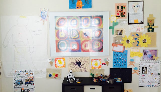 A scotch-taped wall with a child's drawings behind a desk with toys on it.