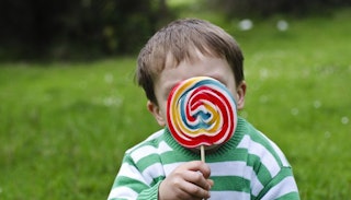 A toddler boy wearing a green-and-white striped long sleeve shirt and licking a popsicle in a green ...