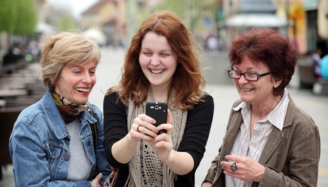 A red-haired younger woman taking a selfie with her two aunts 