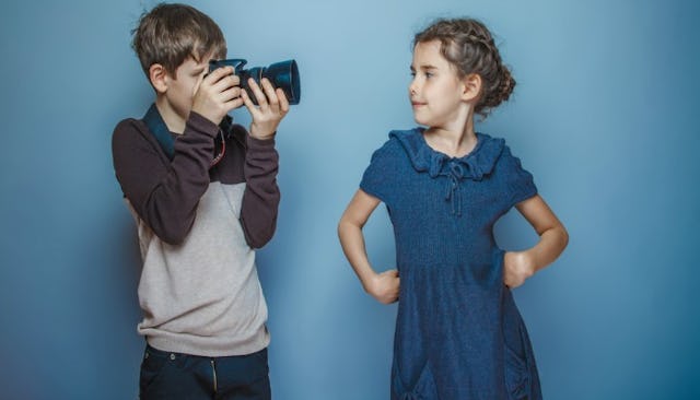 A boy taking a photo of a girl in a blue dress with a teal background