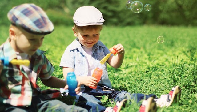 Two sons with hats wearing colorful clothes sitting on the grass, playing and smiling