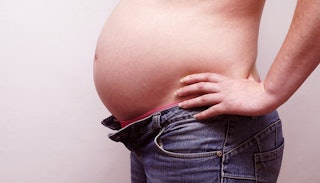 A pregnant woman standing in jeans with the top button unbuttoned 
