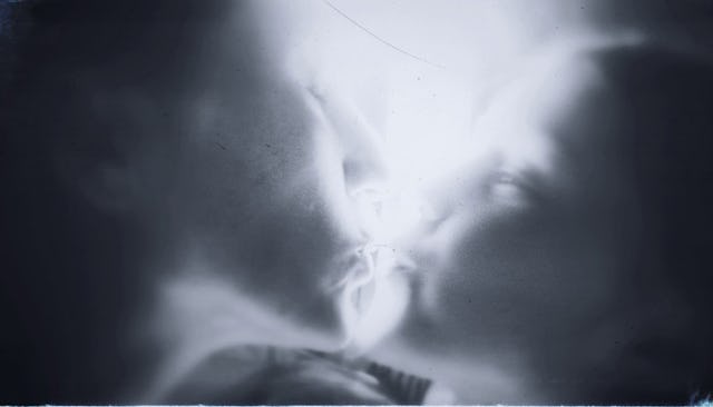 A heavily blurred black-and-white image of a mother kissing her daughter goodbye