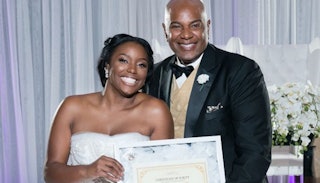 A bride and her father both posing and smiling for a picture while holding a "purity certificate"