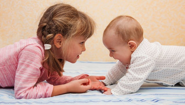 A firstborn daughter wearing a pink shirt while lying down, looking at her smiling newborn sibling