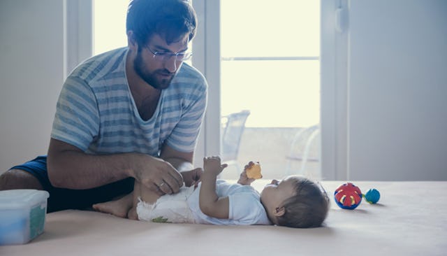 A dad in a white-grey striped shirt changing his baby's diaper