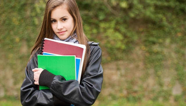 A sixteen-year-old girl holding her school notebooks in green, blue and brown color and standing in ...