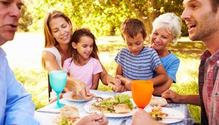 Two kids with parents and grandparents having food at the picnic table