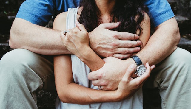 Man hugging his wife from behind while they're sitting on steps in support of her speaking publicly ...