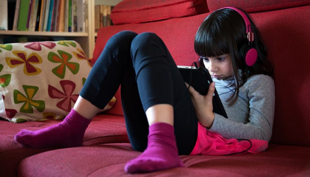 A dark-haired girl with pink headphones wearing a grey shirt, black leggings, and purple socks playi...