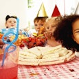 Five kids at a child’s birthday party wearing birthday hats while smiling and eating at the table