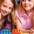 Two little girls ready to play a board game smiling and happy and one of them is holding her thumb u...