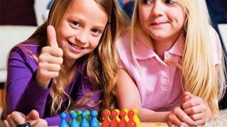 Two little girls ready to play a board game smiling and happy and one of them is holding her thumb u...