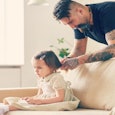A father braining his daughter's hair on a beige couch