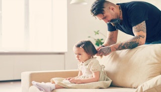 A father braining his daughter's hair on a beige couch