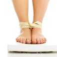 A girl on a weight scale with her legs tied together by a measuring tape