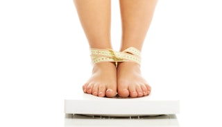 A girl on a weight scale with her legs tied together by a measuring tape