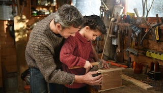 A man and his son making something out of wood, in their garage.