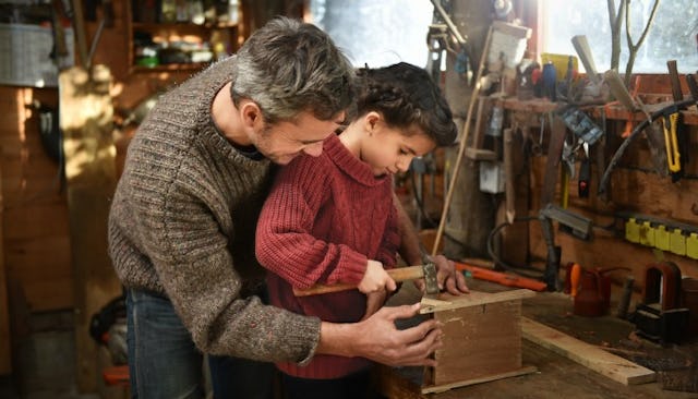 A man and his son making something out of wood, in their garage.