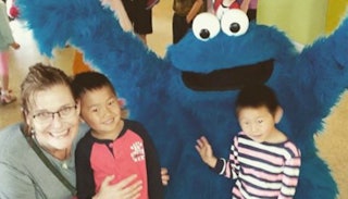 A woman with her two adopted kids taking a photo with The Cookie Monster.