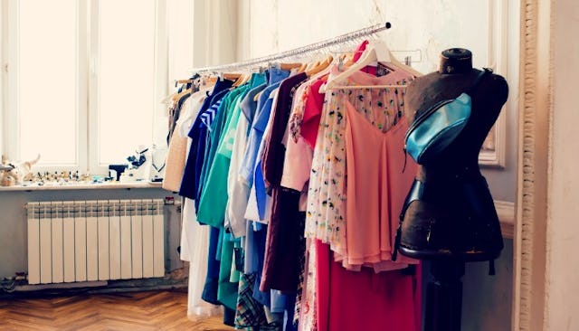 A rack with many different pieces of clothing on it next to a black mannequin with a blue bag on it ...