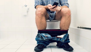 Man using a cellphone while sitting on a toilet in the bathroom that he uses as a man cave