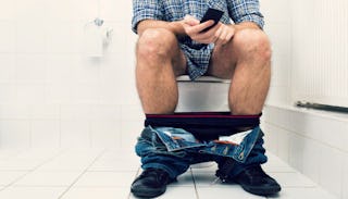 Man using a cellphone while sitting on a toilet in the bathroom that he uses as a man cave