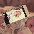A woman holding her phone and taking a picture of a newborn baby
