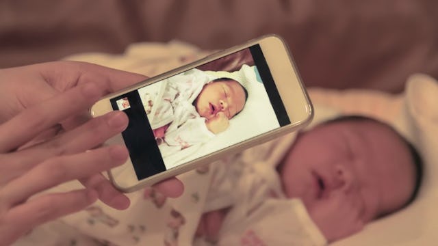 A woman holding her phone and taking a picture of a newborn baby