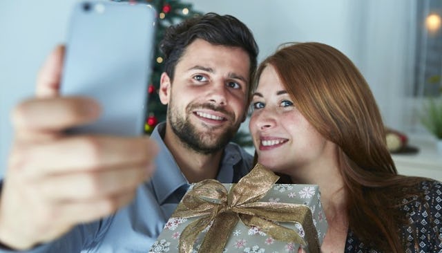 A man talking a selfie with a woman while she's holding a holiday gift