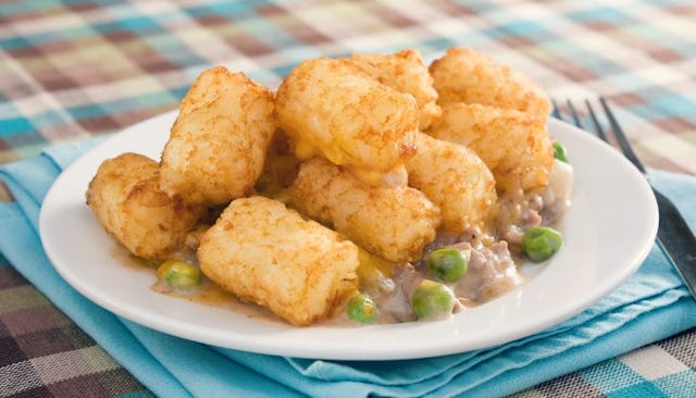 Tater tots with peas served on a white plate on a table covered with a checkered table cloth