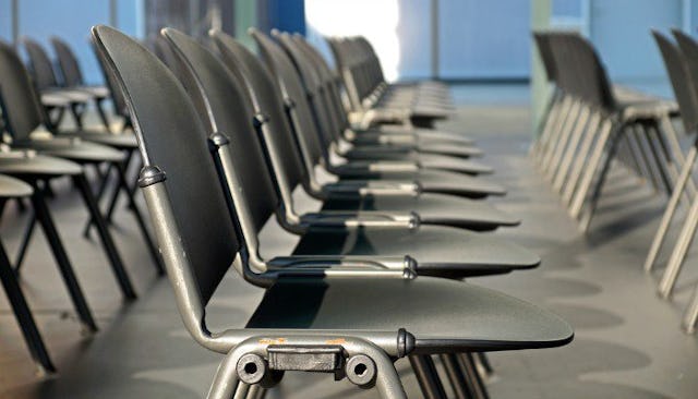 Multiple rows of gray metal chairs in a room with a gray floor and blue background prepared for an A...
